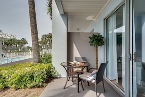 Een balkon met een glazen deur, een kleine tafel met stoelen, en een zwembad op de achtergrond.