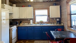 Une cuisine de taille réduite avec des meubles blancs, un plan de travail bleu, une cuisinière, un four à micro-ondes et un ventilateur de plafond.