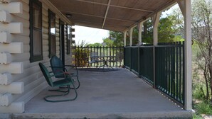 Une véranda couverte avec une chaise berçante et une table, un revêtement en bois et une clôture verte.