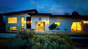 A modern two-story house with a flat roof, large windows, and a well-lit entrance. - Mid Century Modern - Direct Park Access with Stargazing Patio (Joshua Tree)