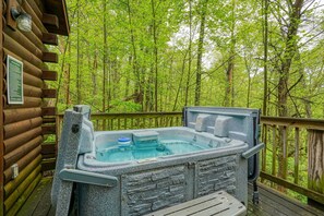 Un bain à remous en pierre, installé sur une terrasse en bois, entouré d’une forêt.
