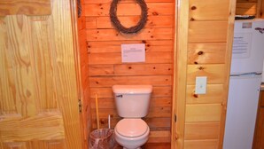 Een houten badkamer in een blokhut, met een toilet, een prullenbak en een krans aan de muur.