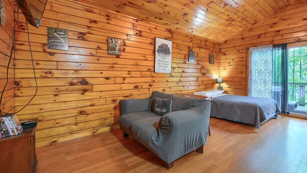 Een gezellig vakantiehuisje met houten wanden en vloeren, een bank, een bed en een kleine tafel met een lamp.
