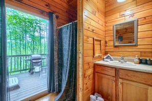 Een houten badkamer met een houten wastafel, een spiegel en uitzicht op een balkon met een barbecue en stoelen.