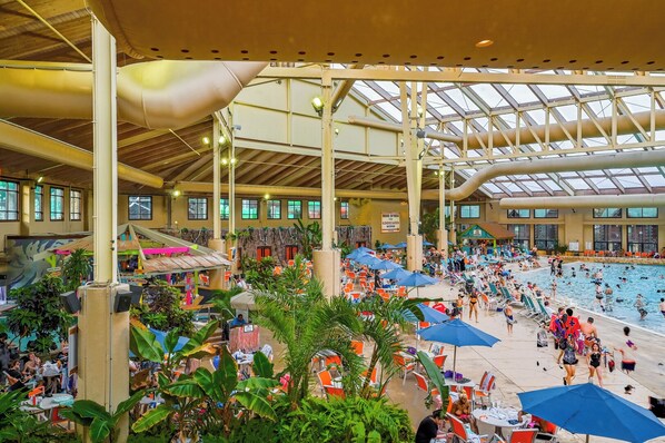 Ein Hallenbad mit mehreren Bahnen, umgeben von Liegestühlen und Sonnenschirmen.