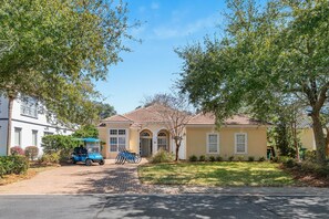 A residential house with a paved driveway, a golf cart, and bicycles parked outside.