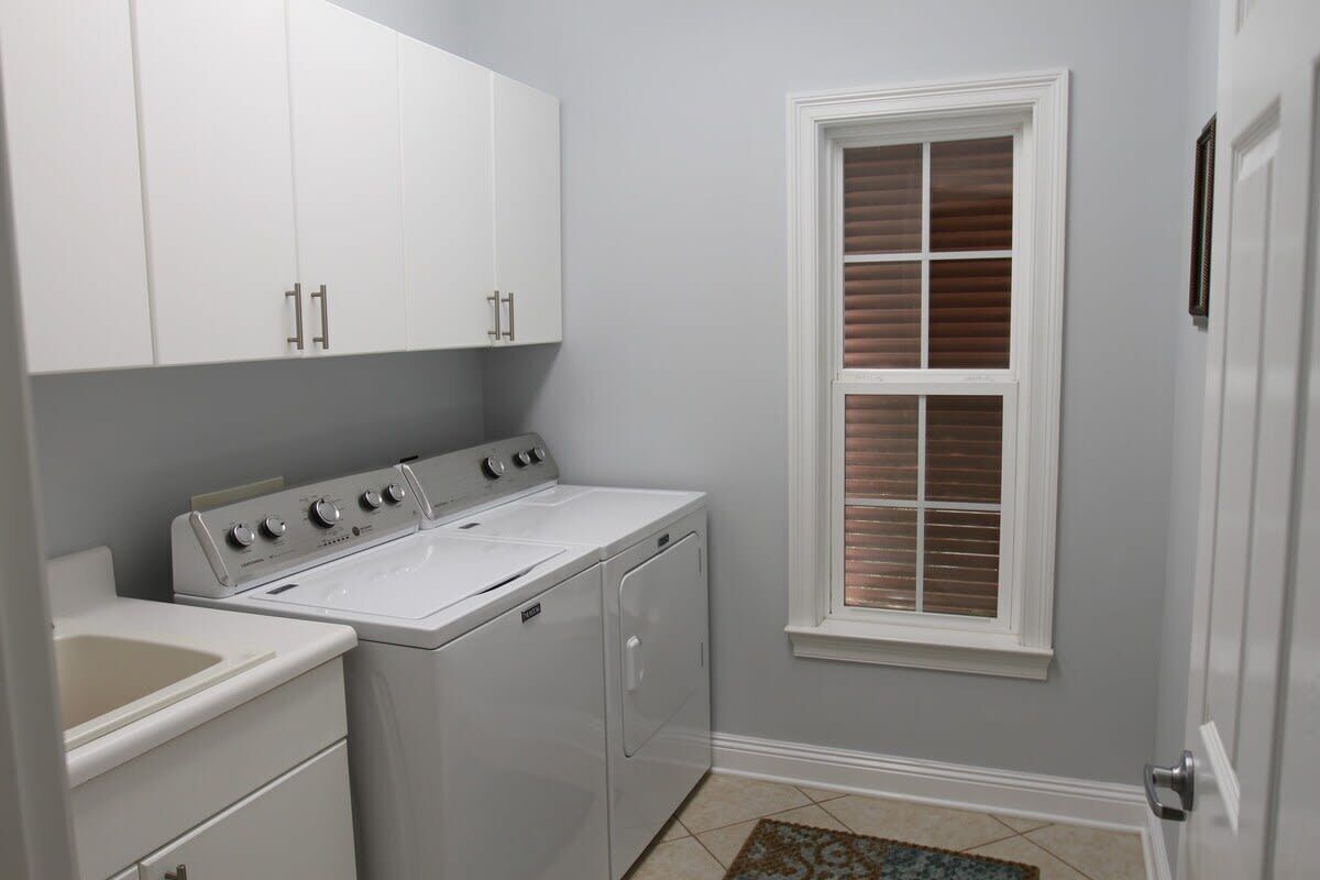 A laundry room with a washer and dryer, cabinets, a window with blinds, and a tiled floor.
