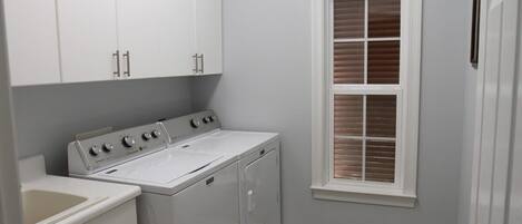 A laundry room with a washer and dryer, cabinets, a window with blinds, and a tiled floor.
