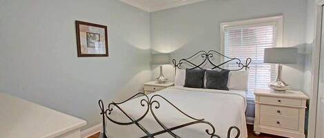A bedroom with a bed, nightstands, a ceiling fan, a window with blinds, and a framed picture on the wall.