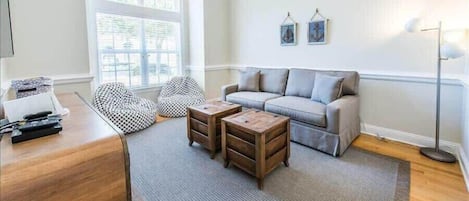 A living room with a sofa, two wooden side tables, a patterned bean bag, and a floor lamp.