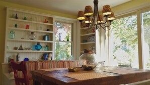 Un coin repas avec une table en bois, une chaise rouge, une bibliothèque remplie de divers objets et un lustre.