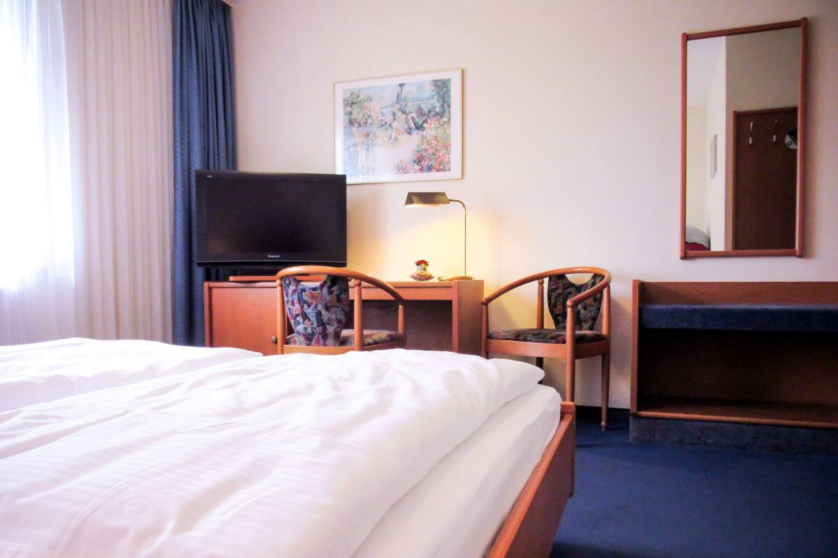 Ein Hotelzimmer mit einem Bett, einem Fernseher, einem Schreibtisch mit Lampe und einem Sessel.