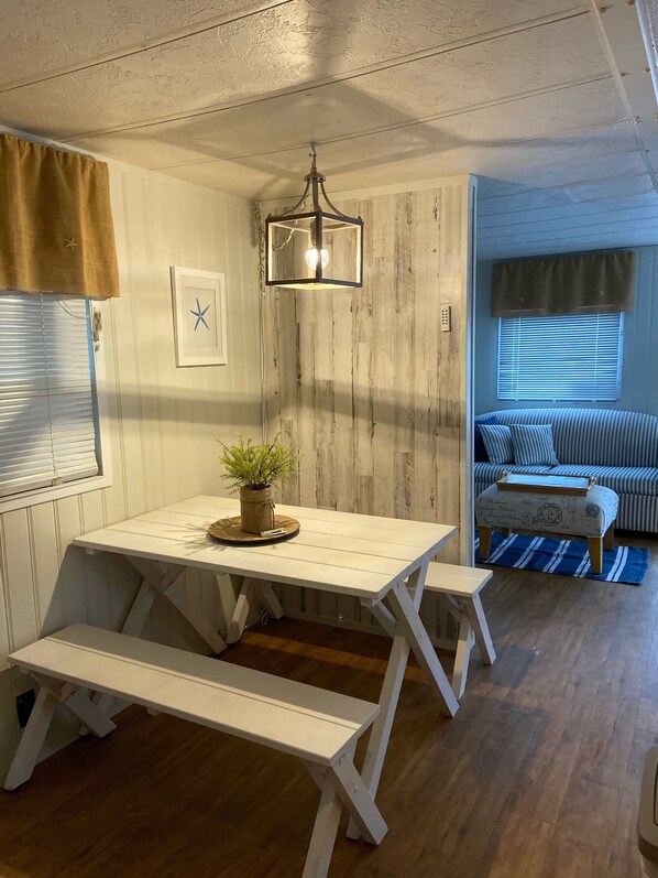 Une pièce chaleureuse avec une table en bois, des bancs, un luminaire suspendu, un canapé à rayures et une fenêtre avec des stores.