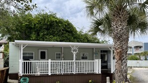 Ein kleines, eingeschossiges Mobilheim mit weißer Veranda und einer kleinen Terrasse.