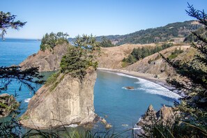 A coastal landscape with a rocky cliff, beach, and forested hills.