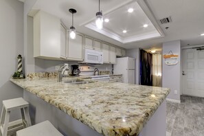 A modern kitchen with a large island, white cabinets, and pendant lighting. - From your condo to the beach in seconds!! (Indian Rocks Beach)