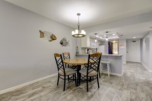 A dining area with a wooden table and chairs, a chandelier, and decorative wall art. - From your condo to the beach in seconds!! (Indian Rocks Beach)