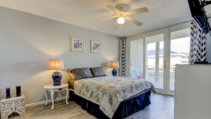 A bedroom with a bed, two bedside tables, a ceiling fan, and a large window.