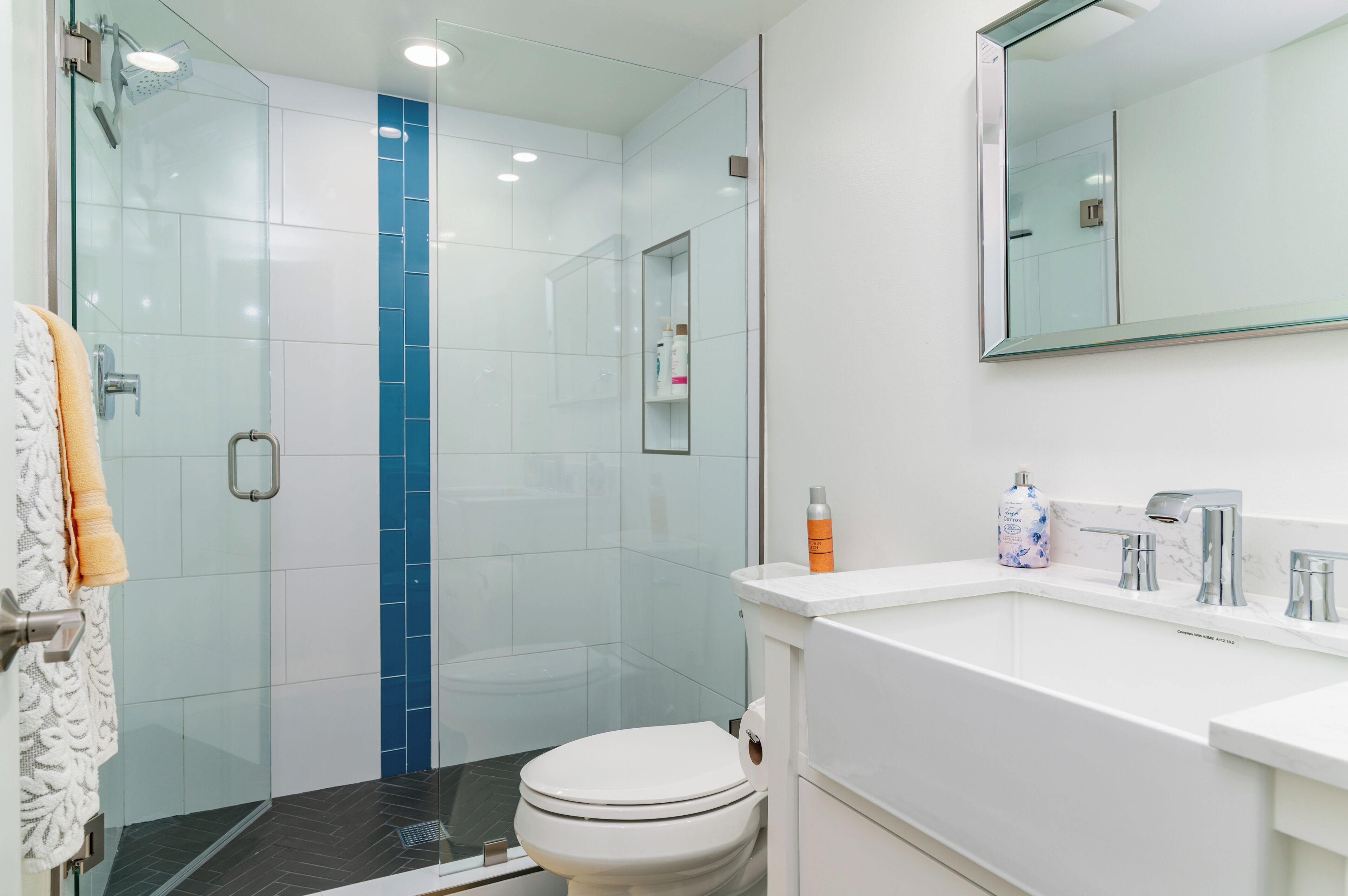 A modern bathroom with a glass shower enclosure, a white toilet, and a white sink with a mirror above it.