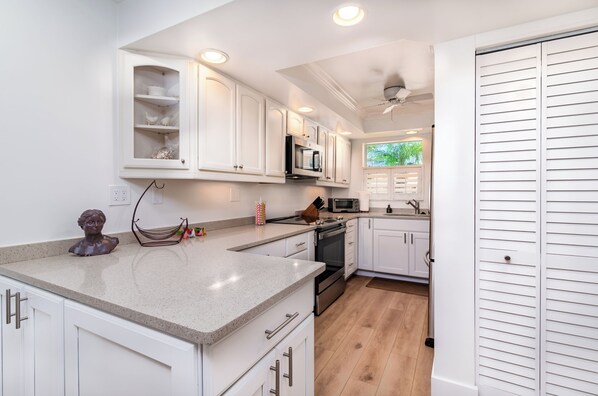 A modern kitchen with white cabinetry, a granite countertop, stainless steel appliances, and a view of the outdoors through a window.