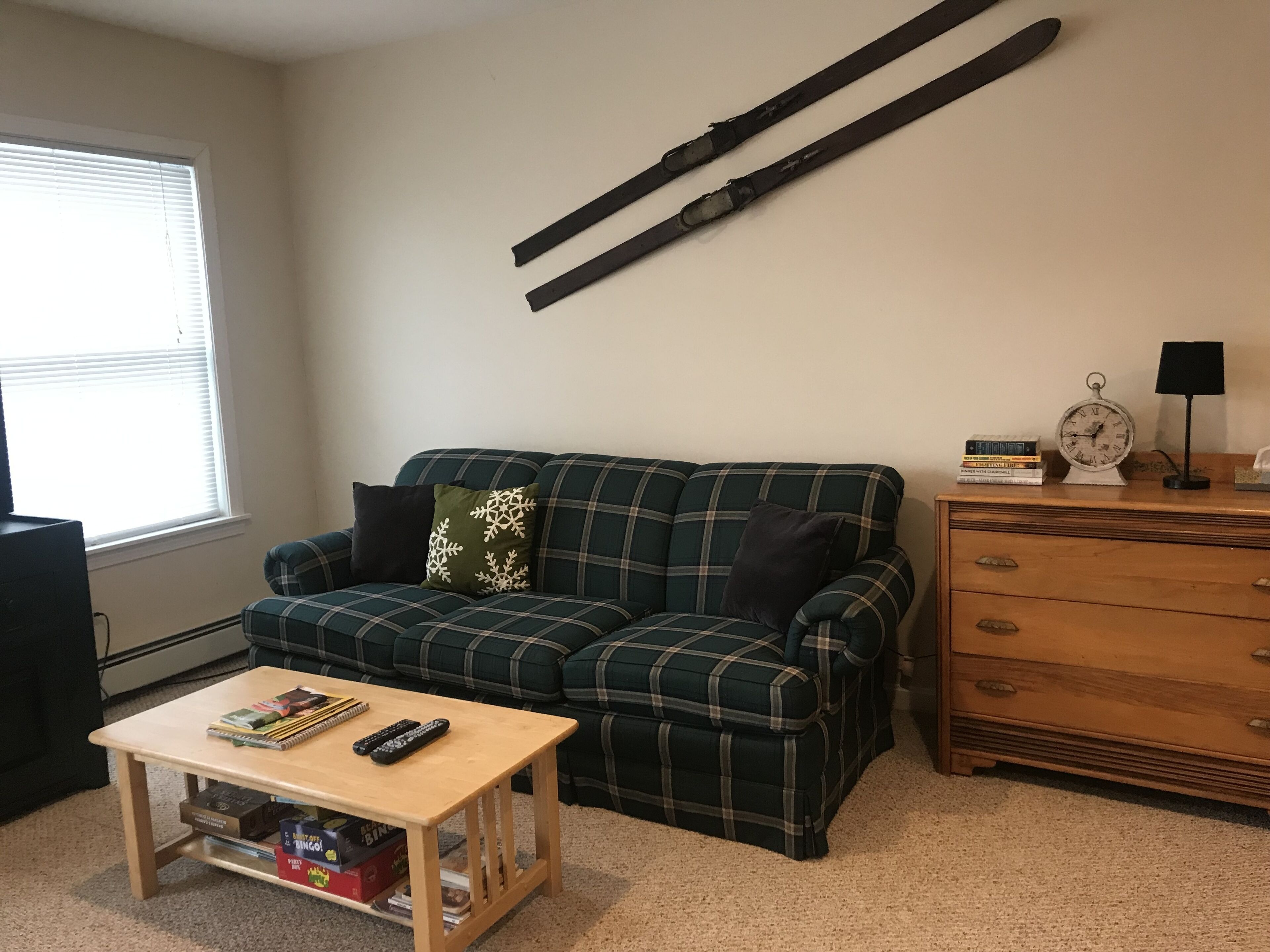 Una sala de estar con un sofá a cuadros, una mesa de centro de madera y un aparador con un reloj y una lámpara.