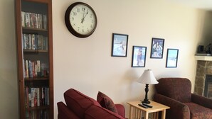 Un salon avec un canapé rouge, une bibliothèque en bois, une horloge murale, des tableaux encadrés et une cheminée.
