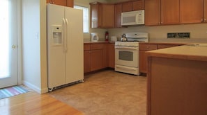 A kitchen with a dishwasher and microwave, wooden cabinets, a stove, and a refrigerator. - Pleasant Mountain Condo Ski in Ski out (Bridgton)