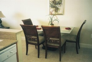 Un coin repas comprenant une table et quatre chaises, une plante en pot et un tableau encadré accroché au mur.