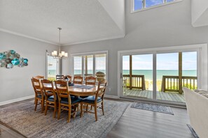 A dining area with a wooden table and chairs, large windows with blinds, and a view of the ocean. - Namaste at the Beach Oceanfront House, Dog Friendly, Private Beach Access! (Kure Beach)