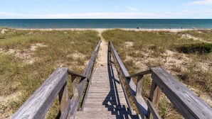 Une promenade en bois qui mène à une plage, avec l’océan en arrière-plan.