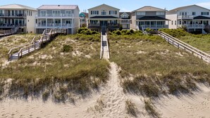 Une propriété située en bord de mer, comprenant plusieurs maisons, un sentier sablonneux menant à la plage et un escalier en bois.