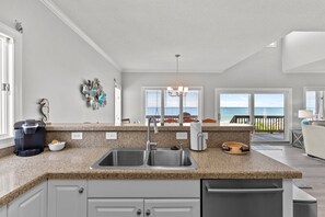 A kitchen with a double sink, granite countertop, and a view of the ocean through large windows. - Namaste at the Beach Oceanfront House, Dog Friendly, Private Beach Access! (Kure Beach)