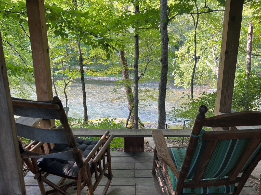 A wooden deck with two rocking chairs overlooking a river.