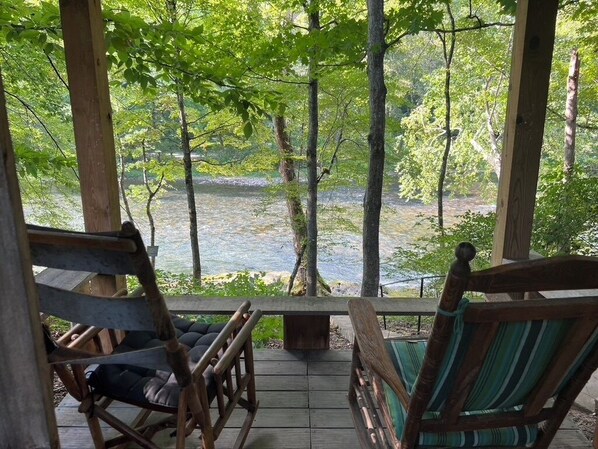 Une terrasse en bois avec deux fauteuils à bascule donnant sur une rivière.