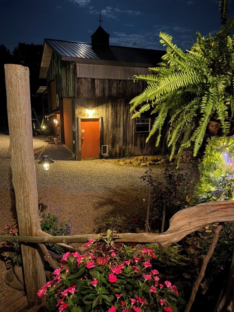 A rustic wooden building with a metal roof, surrounded by gravel and flowering plants.