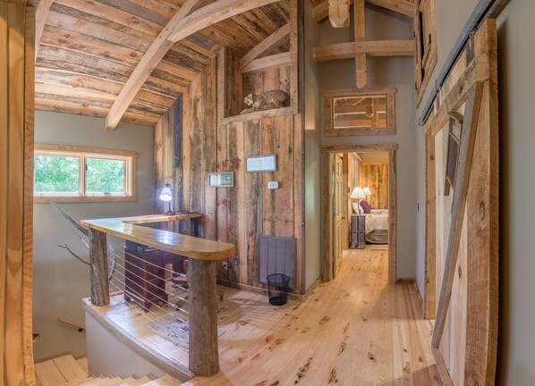 Un interior rústico de madera con una escalera, una mesita y una cama al fondo.