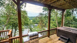 Une terrasse couverte avec un barbecue et un coin salon donnant sur une rivière bordée d’arbres.