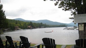 Outdoor seating with chairs and tables facing a lake, surrounded by trees and mountains.