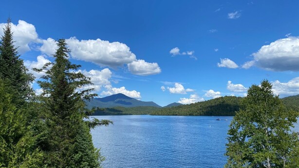 A lake surrounded by dense forest and mountains under a clear blue sky.