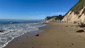 A beach with a clear sky, a sandy shore, and a steep cliff with vegetation.