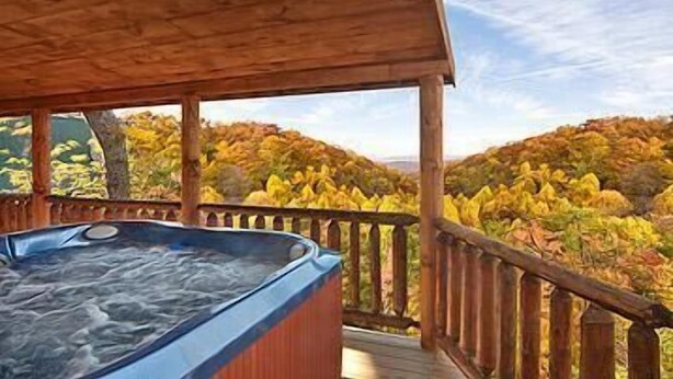Terraza de madera con un jacuzzi, con vistas a un área boscosa con follaje otoñal.