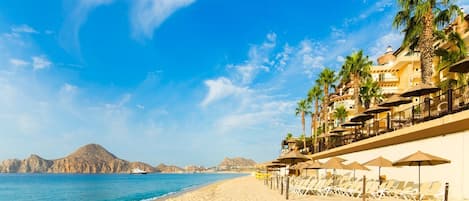 Relax on the beach with ocean views and a mountain backdrop, surrounded by sun loungers and umbrellas.