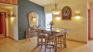 Uma área de refeições com mesa de madeira e quatro cadeiras, um lustre e um quadro floral na parede.