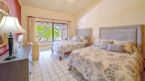 Quarto de hotel com duas camas, uma escrivaninha, uma luminária e uma janela com cortinas.