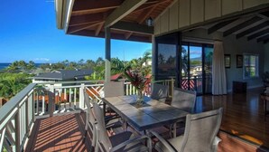 A covered outdoor area with a table and chairs, a view of the ocean, and a building with large windows. - Oceanview, Walk to Poipu Beach, AC, Private Lanai! (Koloa)