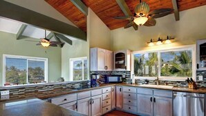 A kitchen with wooden beams, a ceiling fan, a large window with a view, and built-in cabinets. - Oceanview, Walk to Poipu Beach, AC, Private Lanai! (Koloa)