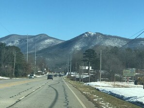 A road with vehicles, a sign for a steak house, and snow-covered mountains in the background. - Pretty Fawn Place, Wow View, Clean! Dogs Welcome. Hot Tub. Convenient To Town. (Hiawassee)