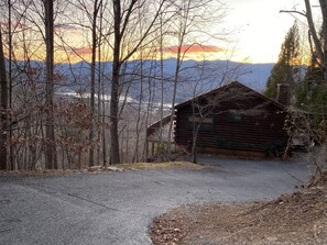 A rustic cabin with a wooden exterior, surrounded by trees and a mountain backdrop.
