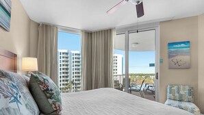 Ett hotellrum med en stor säng, en balkong med stolar och utsikt över höga byggnader.