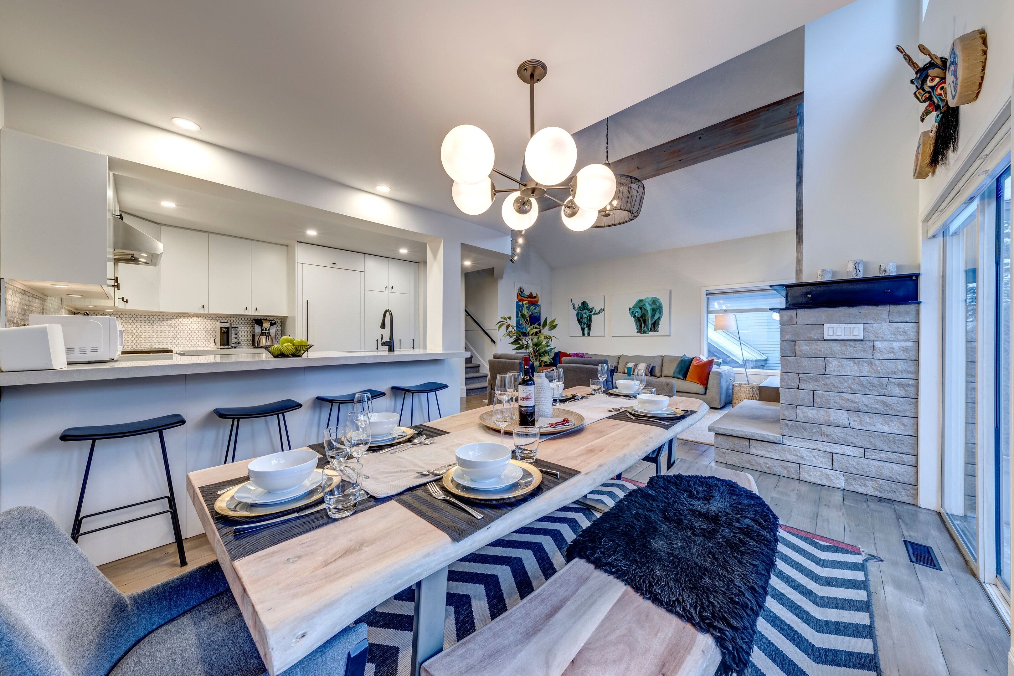 Een moderne keuken met witte kasten, een eethoek met een houten tafel voor vier personen, en een zithoek met een bank en een open haard.